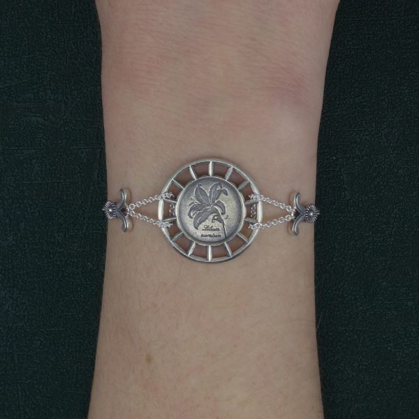 Bracelet rond à motif botanique de lys façon herbier dans un cadre d'inspiration architecture en argent de fabrication Française porté sur poignet | Res Mirum