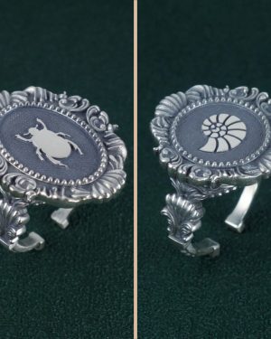 Bague scarabée noir sacré des égyptiens dans son cadre ovale mouluré, esprit baroque et musée en argent massif & Bague nautilus, ammonite ou coquillage, entourée d'un cadre baroque dans l'esprit des cabinets de curiosités de la Renaissance vue de côté | Res Mirum